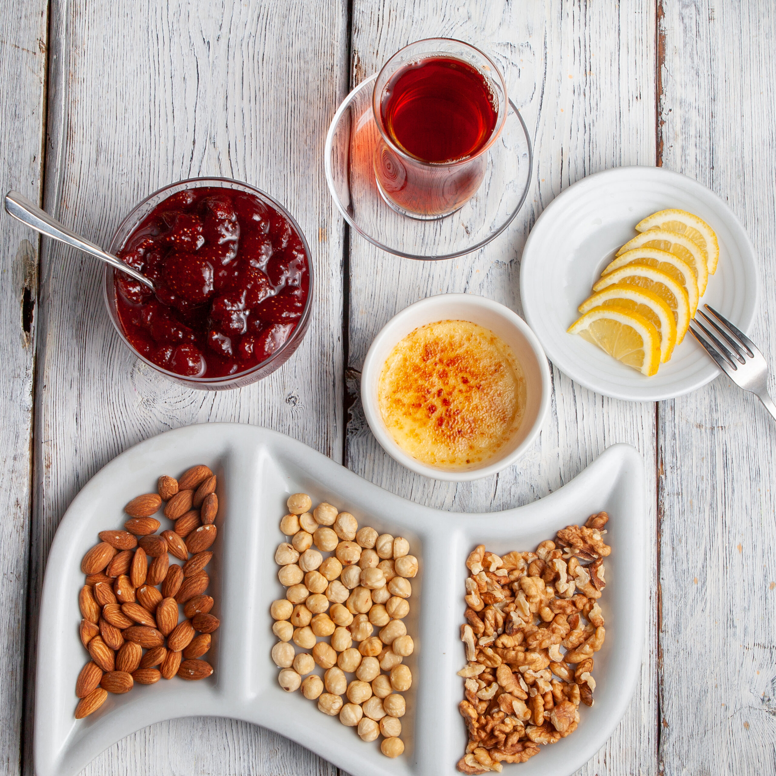 Home top view delicious dessert in plate with tea, nuts, fruit jam, sliced lemons on white wooden background.